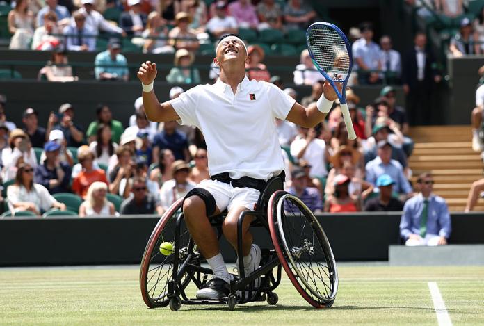 A male wheelchair tennis player celebrating a win on court